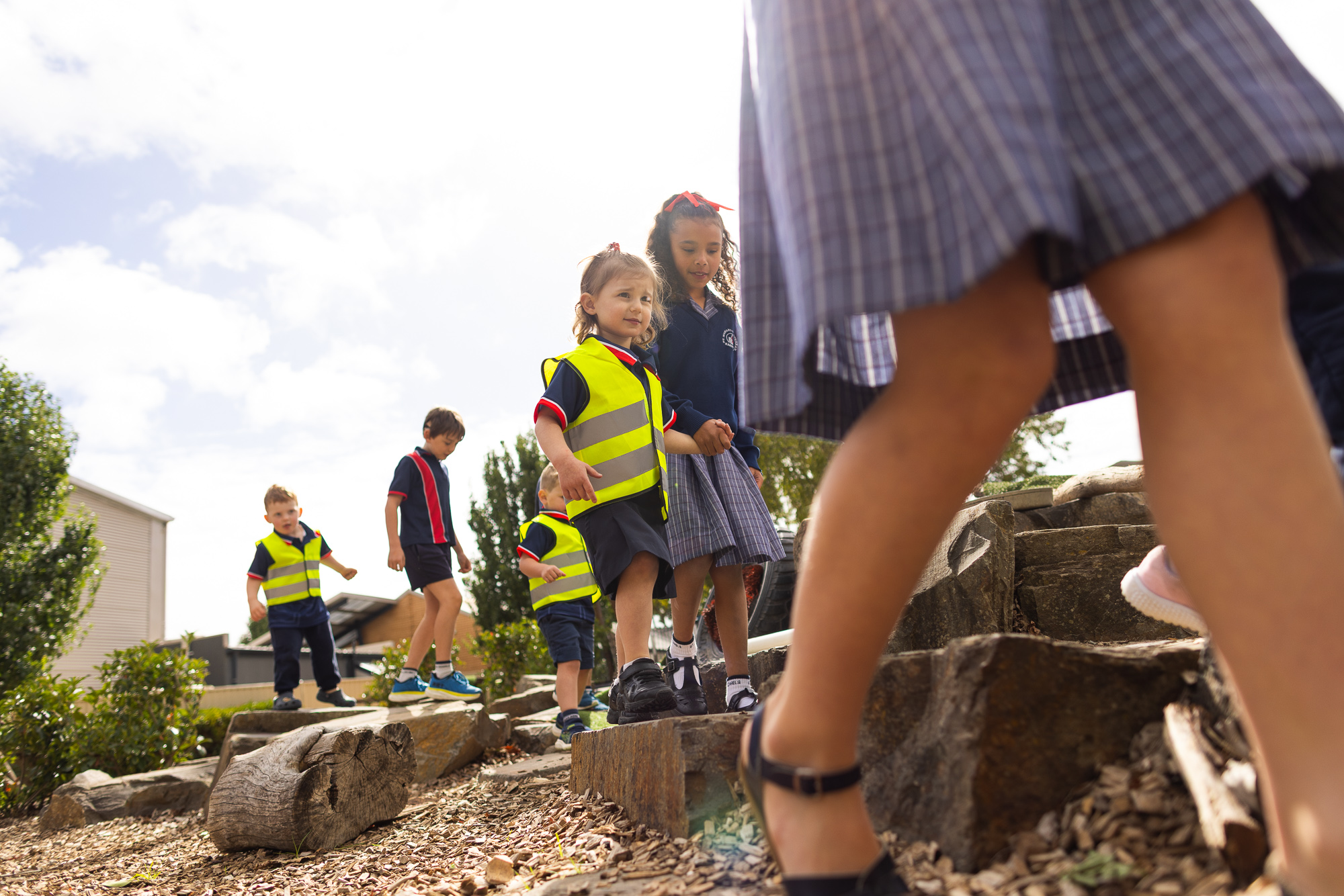 Children in school uniforms exploring an outdoor nature play area with logs and rocks at St Michael’s Lutheran School.