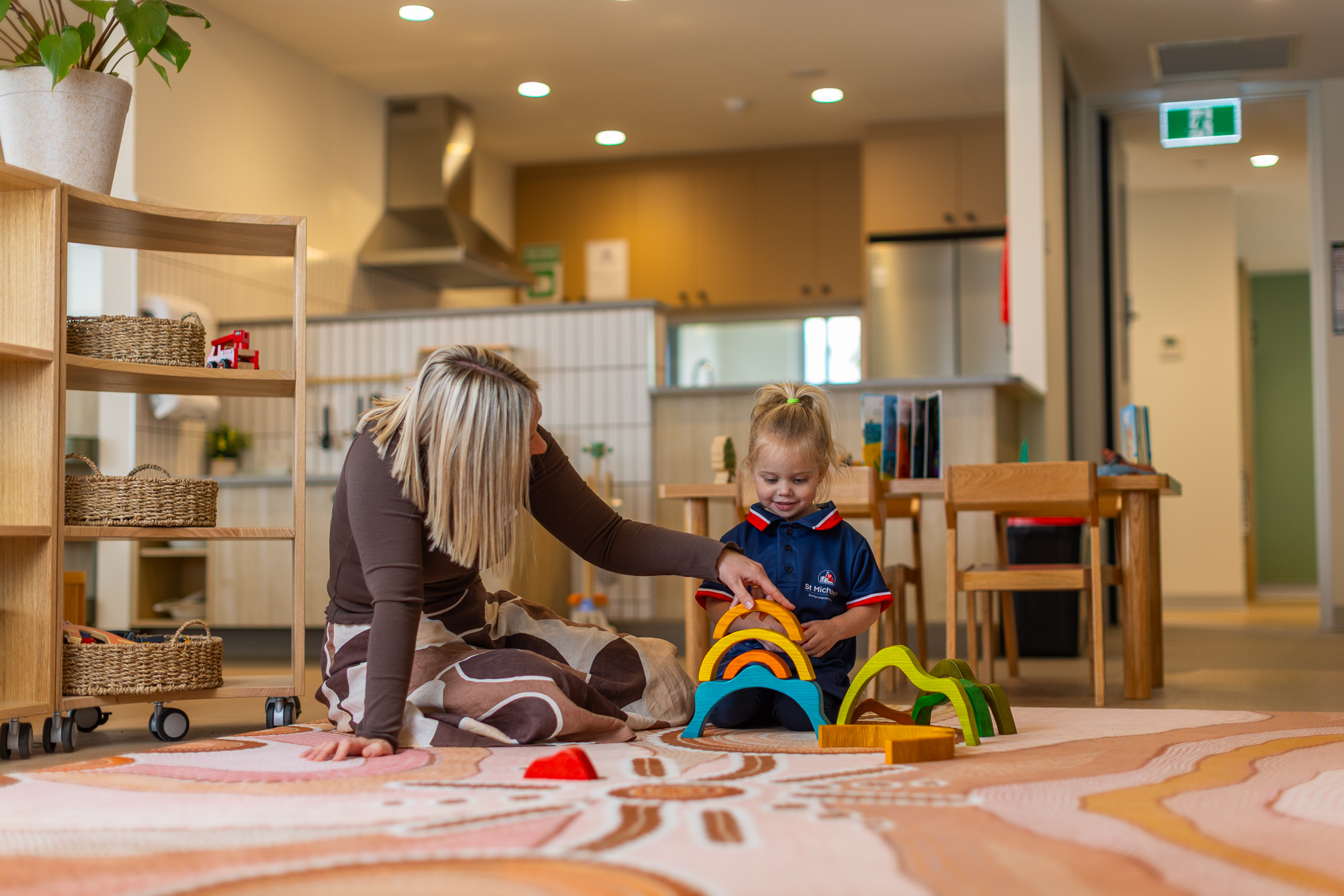 Teacher helping a young student play with colourful wooden toys in an early learning classroom.