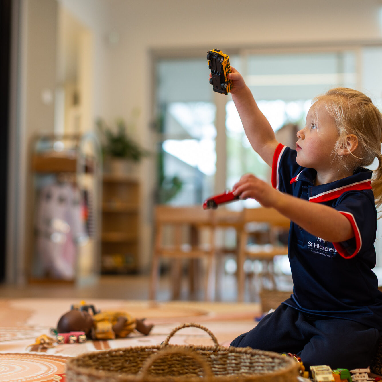 Young child in a St Michael’s Early Learning Centre uniform playing with toy vehicles indoors.