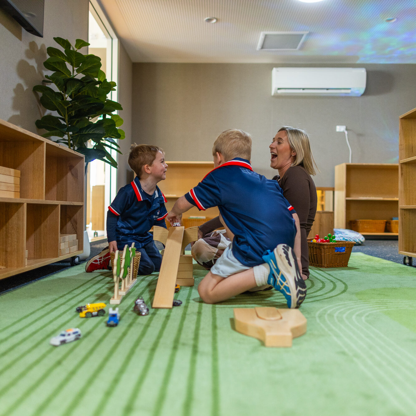 Teacher playing with two students using wooden toys in a colourful classroom.